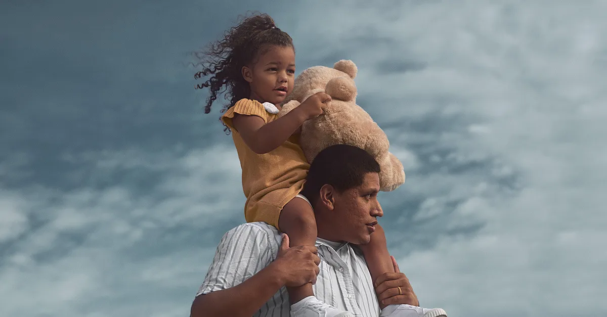 Child holding a stuffed animal while sitting on the shoulders of an adult