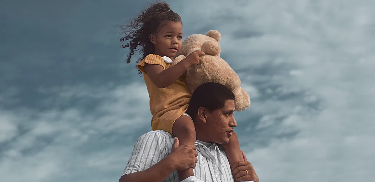 Child holding a stuffed animal while sitting on the shoulders of an adult