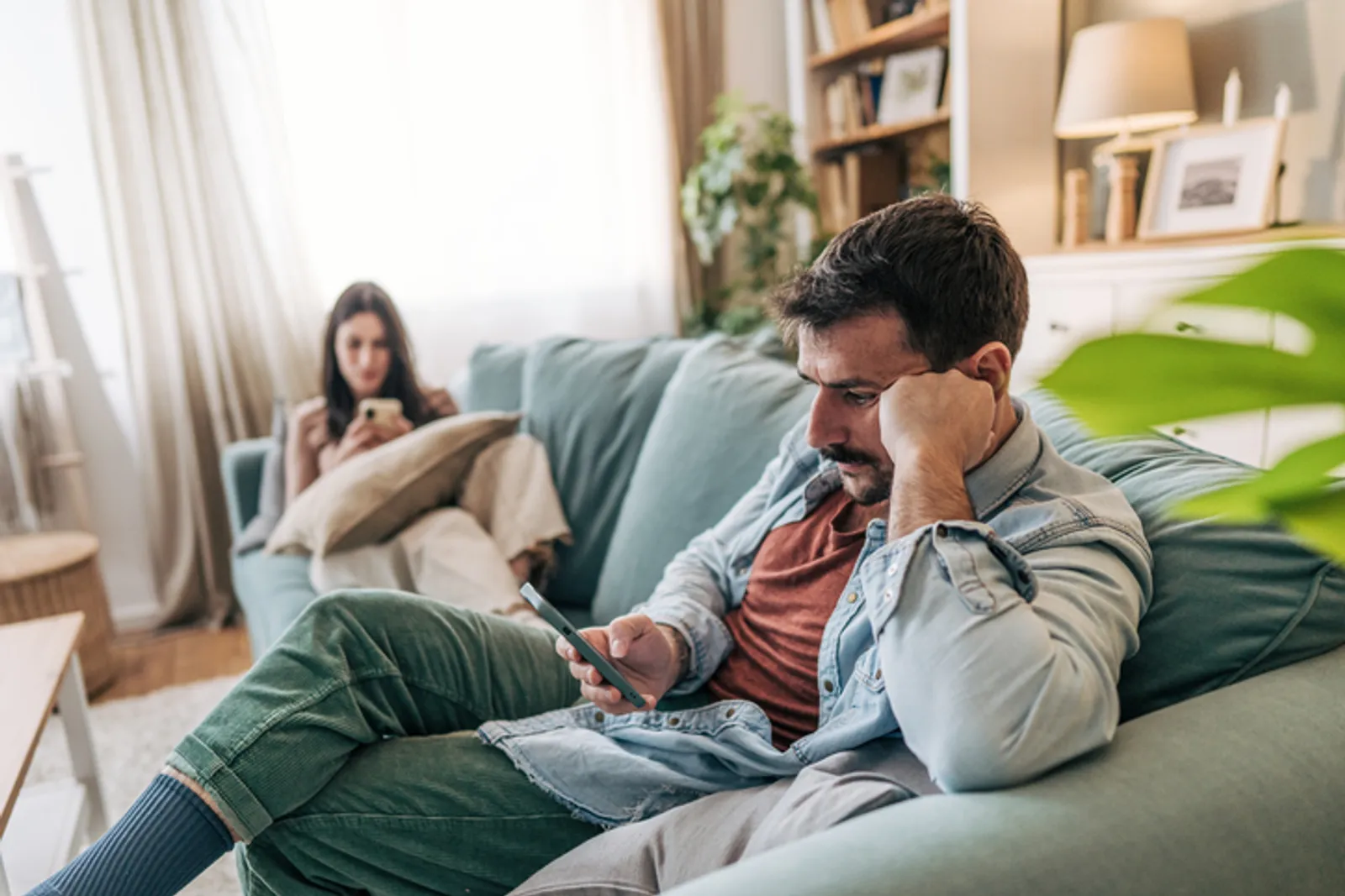 Young couple sitting on the sofa, absorbed in their smartphones, creating a sense of distance and isolation while neglecting meaningful communication in their relationship