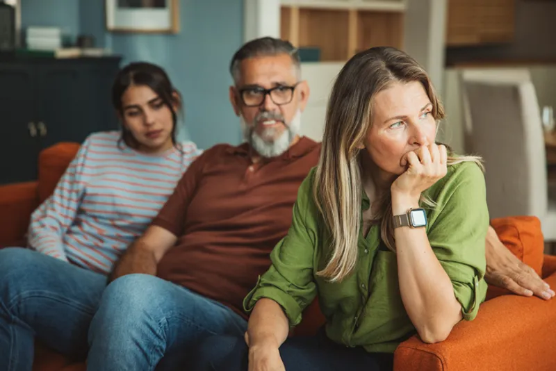 Parents and adult daughter sharing a moment of comfort and emotional support on a sofa.