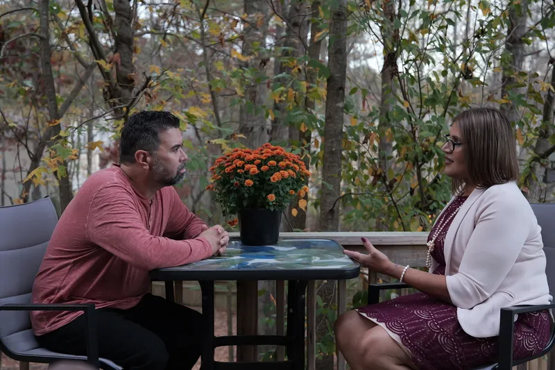 two people sitting and talking at a table outdoors