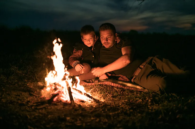 Father and son laying in the grass staring at a bonfire