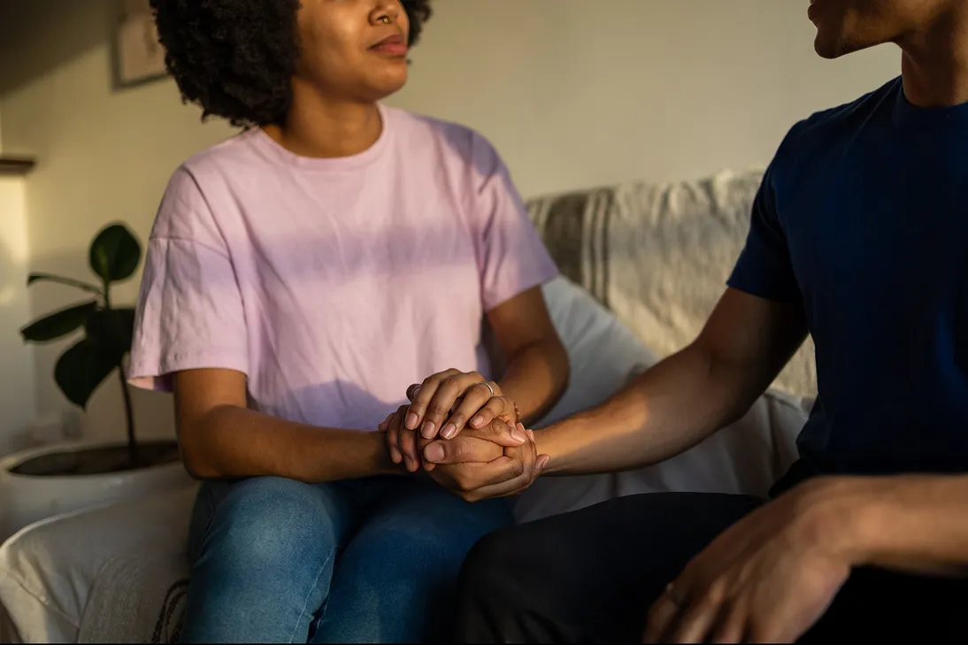 Man and woman holding hands, sitting on the couch